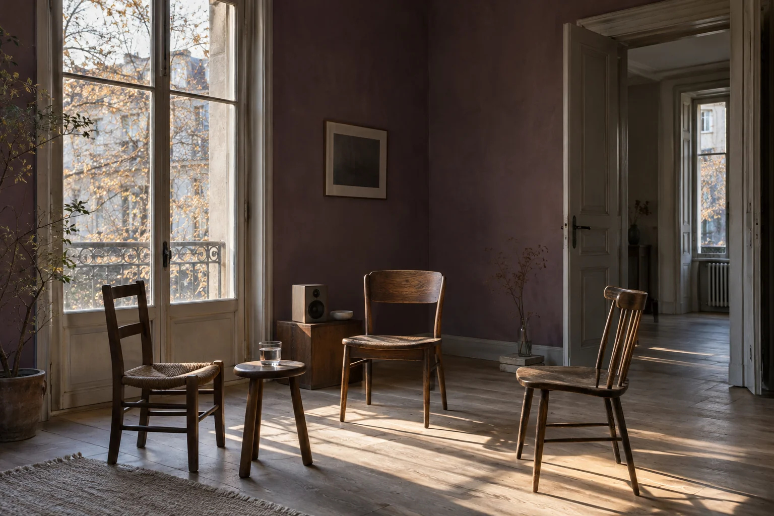 Three mismatched wooden chairs and a speaker beside a window in a warm listening room.